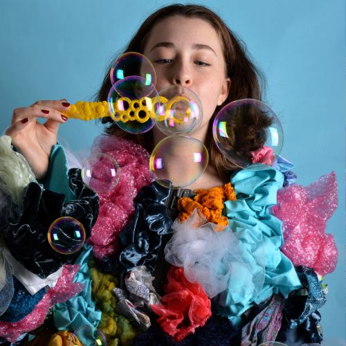 Person blowing bubbles wearing an outfit with various colours
