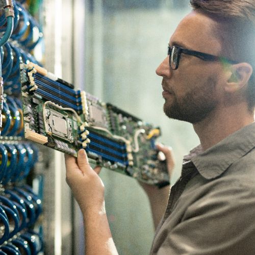 Photo of a person holding up a motherboard in front of a server rack